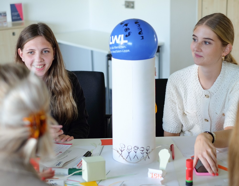 Junge Frauen sitzen an einem Tisch und basteln einen LWL-Turm.
