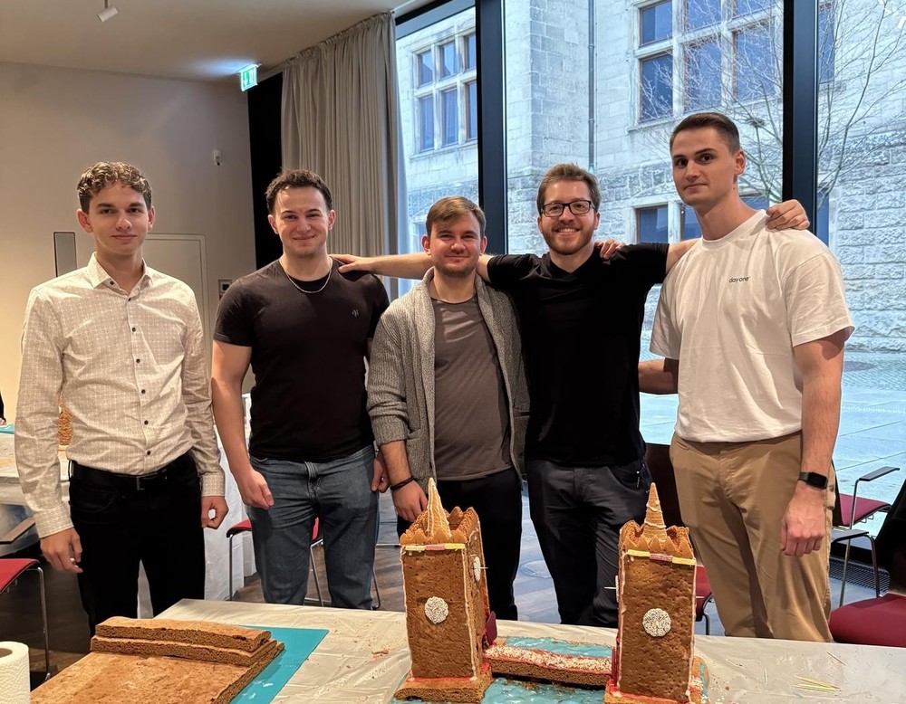Mehrere männliche Auszubildende stehen hinter ihrem selbst gebauten Lebkuchenhaus.