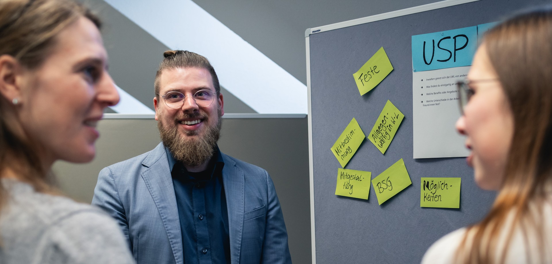 Auszubildender präsentiert etwas vor einer Wand mit vielen Post-it`s und zwei Personen hören zu
