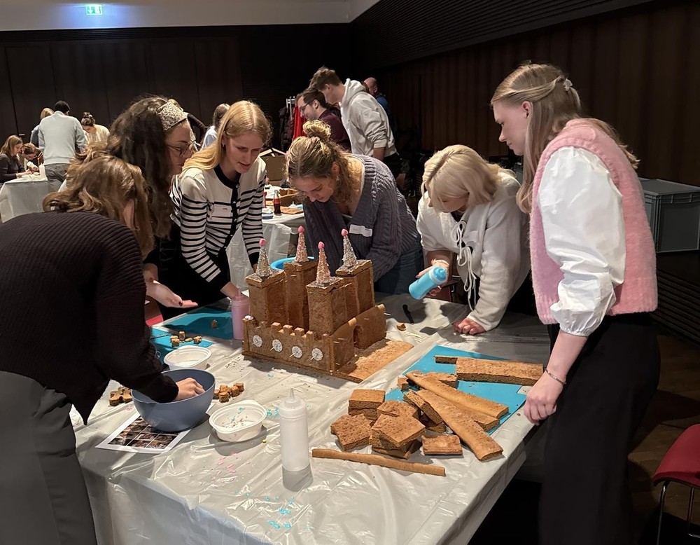 Mehrere Auszubildende stehen um einen Tisch und bauen ein Lebkuchenhaus.