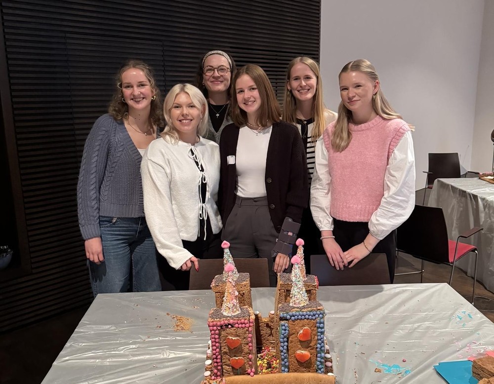 Mehrere weibliche Auszubildende stehen hinter ihrem selbst gebauten Lebkuchenhaus.